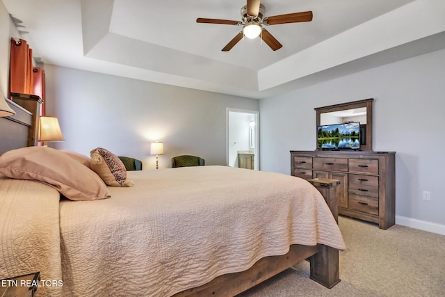 bedroom featuring a ceiling fan, baseboards, a tray ceiling, light carpet, and connected bathroom