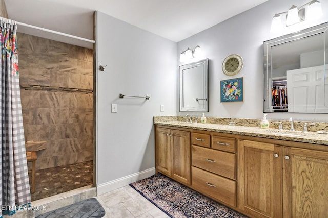 full bath featuring a sink, baseboards, double vanity, and a tile shower