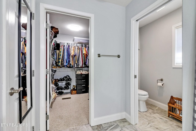 bathroom featuring a walk in closet, baseboards, and toilet