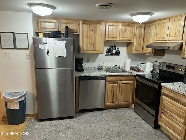 kitchen with under cabinet range hood, appliances with stainless steel finishes, light stone counters, and a sink