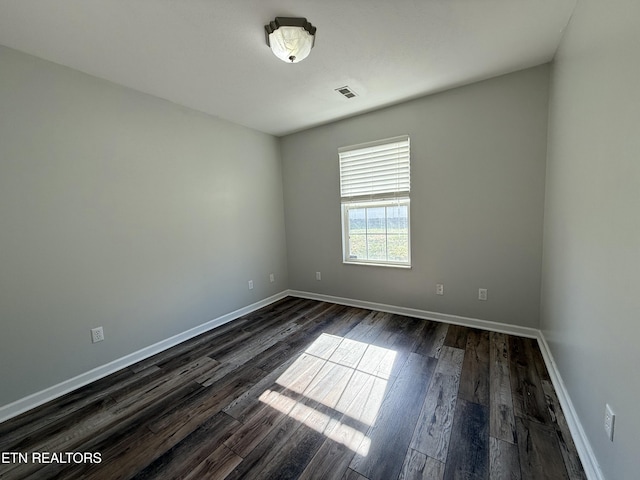 empty room featuring baseboards, visible vents, and dark wood-style flooring