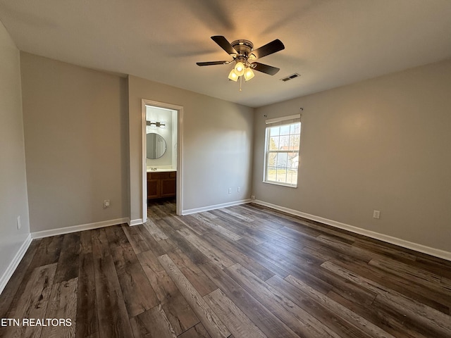 unfurnished bedroom featuring visible vents, dark wood-type flooring, baseboards, ensuite bath, and a ceiling fan