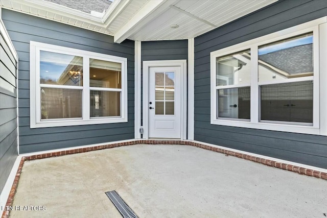 entrance to property with visible vents, a shingled roof, and a patio