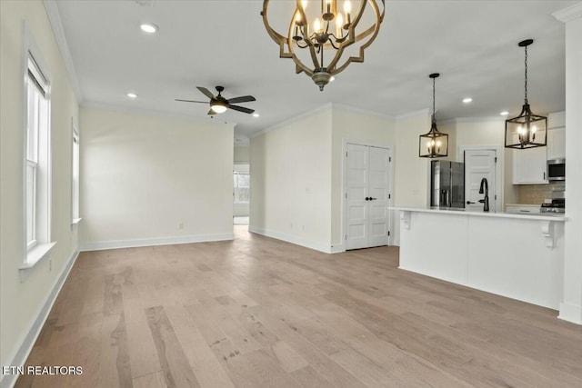 unfurnished living room featuring ceiling fan with notable chandelier, light wood-style floors, baseboards, and ornamental molding