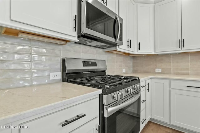 kitchen with decorative backsplash, white cabinets, light stone counters, and appliances with stainless steel finishes