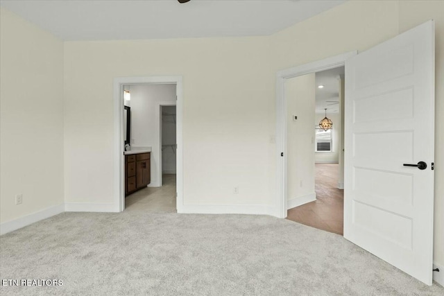 unfurnished bedroom featuring baseboards, light carpet, ensuite bath, and a spacious closet