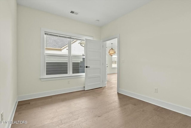 empty room with a chandelier, visible vents, baseboards, and wood finished floors