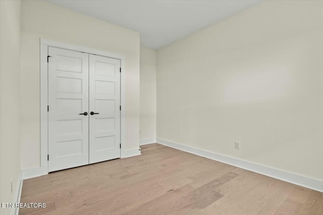 unfurnished bedroom featuring a closet, light wood-style flooring, and baseboards