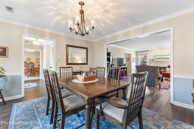 dining room with wood finished floors, visible vents, a textured ceiling, crown molding, and a notable chandelier