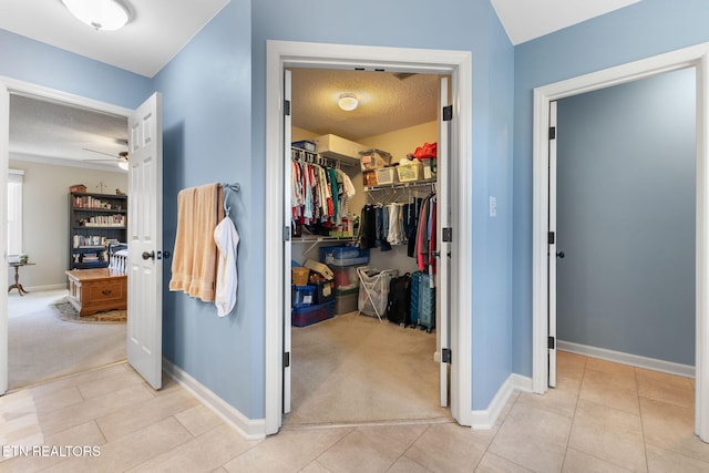 hallway with light tile patterned floors, light colored carpet, baseboards, and a textured ceiling