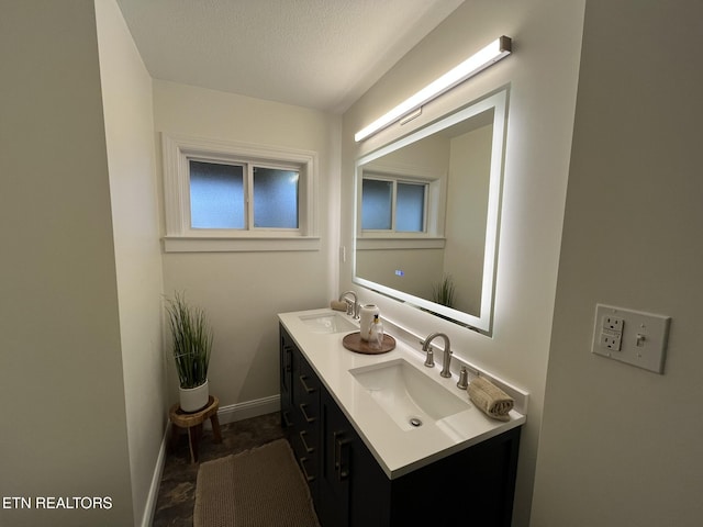 bathroom with a textured ceiling, double vanity, baseboards, and a sink