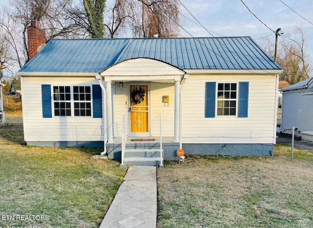 bungalow-style house featuring metal roof, a front yard, and a chimney