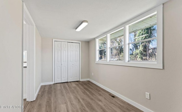 unfurnished bedroom featuring wood finished floors, baseboards, visible vents, and a closet