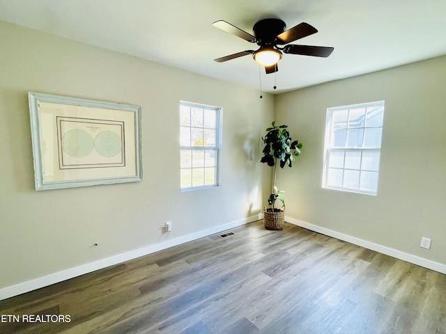 empty room with visible vents, wood finished floors, baseboards, and ceiling fan