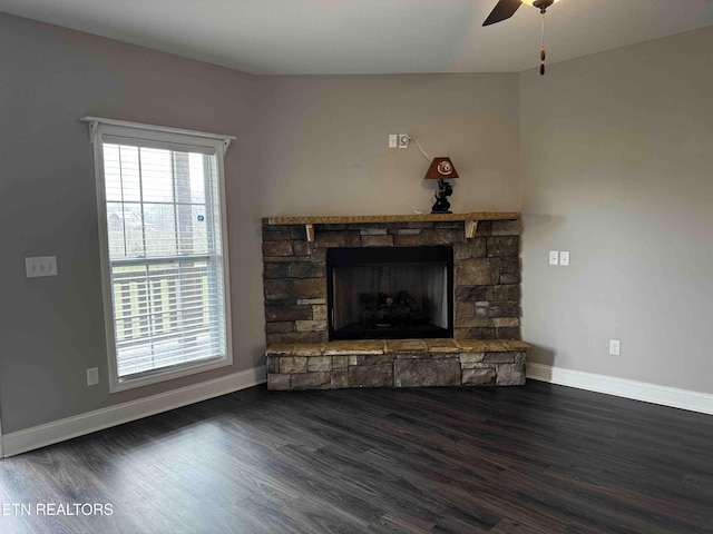 unfurnished living room with a stone fireplace, baseboards, a ceiling fan, and wood finished floors