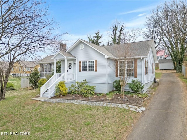 bungalow featuring driveway, roof with shingles, a chimney, and a front lawn