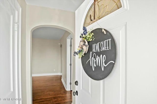 hallway with wood finished floors, arched walkways, and baseboards