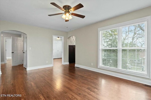 unfurnished living room featuring visible vents, a ceiling fan, wood finished floors, arched walkways, and baseboards