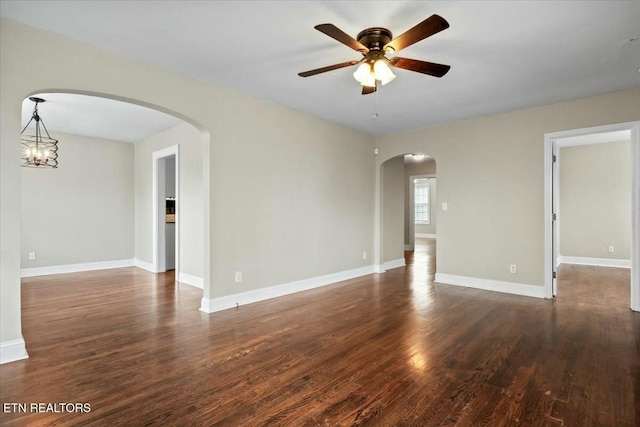 empty room featuring baseboards, wood finished floors, arched walkways, and ceiling fan