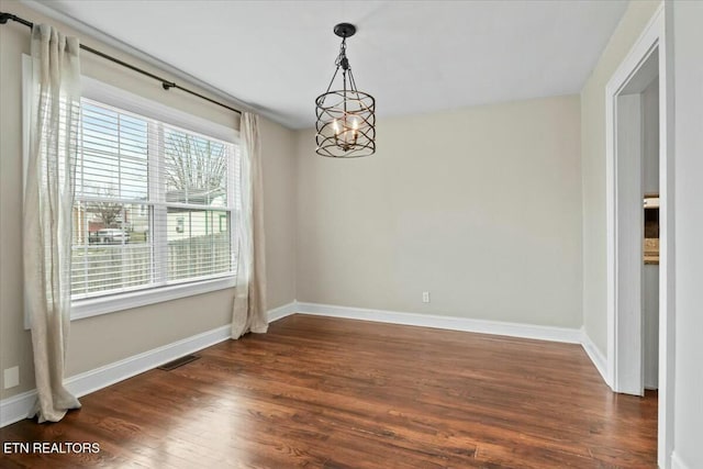 spare room featuring dark wood-style floors, visible vents, a chandelier, and baseboards