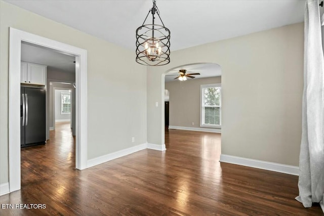 empty room featuring baseboards, arched walkways, dark wood-type flooring, and ceiling fan