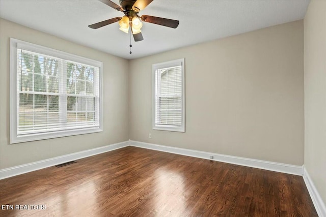 spare room with dark wood-style floors, visible vents, a ceiling fan, and baseboards