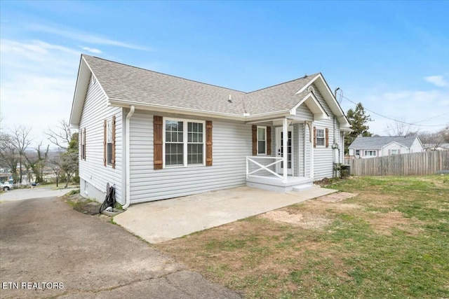 view of front of house featuring a porch, fence, a front lawn, and roof with shingles