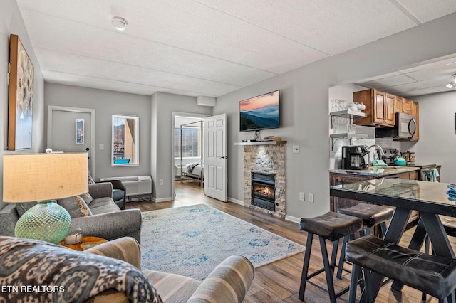 living area with a stone fireplace, a paneled ceiling, baseboards, and wood finished floors