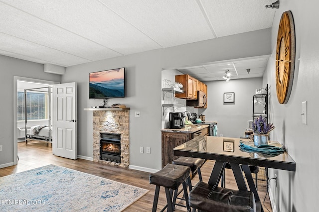 dining area with baseboards, a paneled ceiling, a stone fireplace, and light wood finished floors