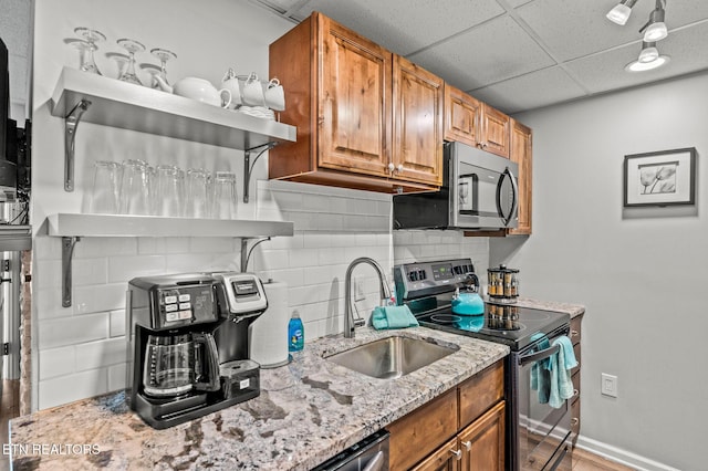 kitchen with stainless steel microwave, light stone counters, decorative backsplash, electric stove, and a sink