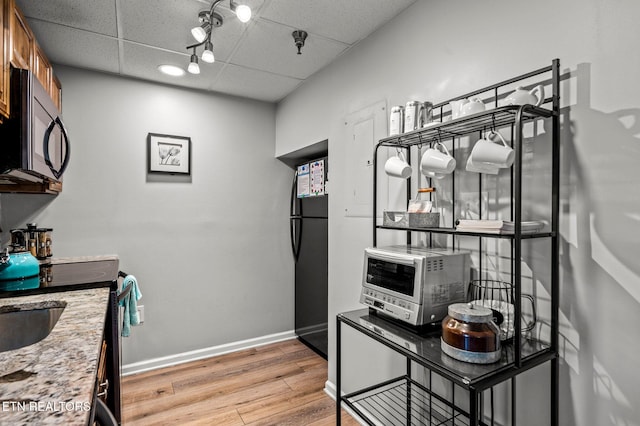 kitchen featuring baseboards, black appliances, a paneled ceiling, and light wood-style floors