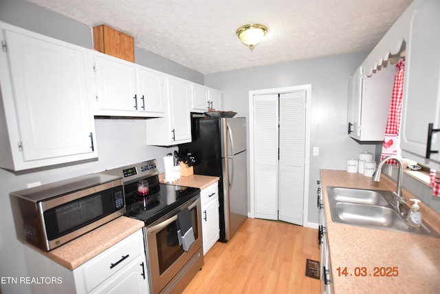 kitchen featuring light wood-type flooring, light countertops, appliances with stainless steel finishes, white cabinetry, and a sink