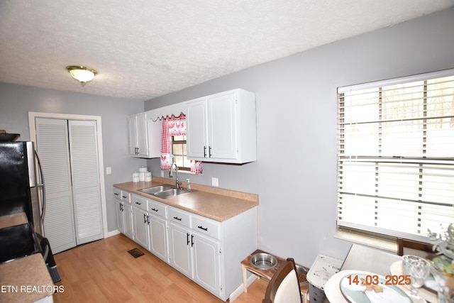 kitchen with freestanding refrigerator, light wood-style floors, white cabinets, a textured ceiling, and a sink