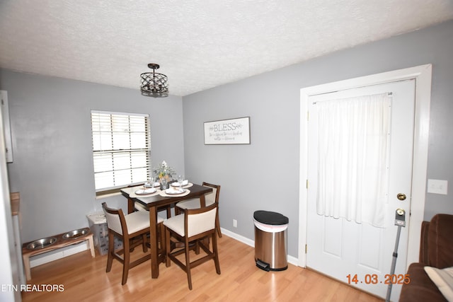 dining space with a textured ceiling, light wood-type flooring, and baseboards