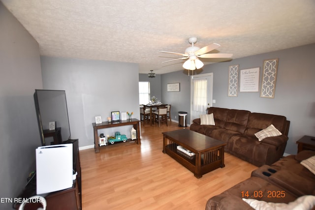 living area with a textured ceiling, light wood-style flooring, and a ceiling fan