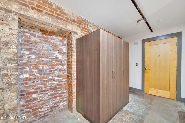 interior space with visible vents, brick wall, unfinished concrete floors, and baseboards