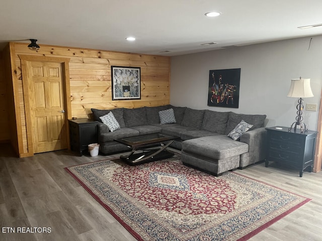 living room with wooden walls, recessed lighting, and wood finished floors