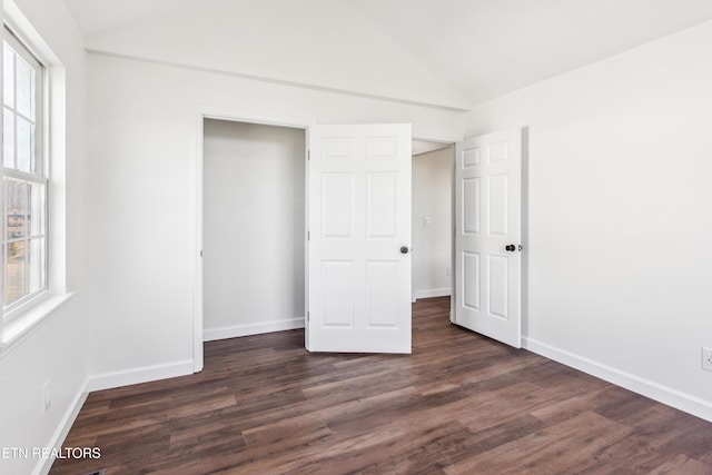 unfurnished bedroom featuring vaulted ceiling, multiple windows, baseboards, and dark wood-style flooring