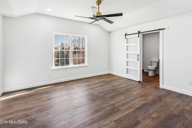 unfurnished bedroom featuring wood finished floors, baseboards, ensuite bath, vaulted ceiling, and a barn door