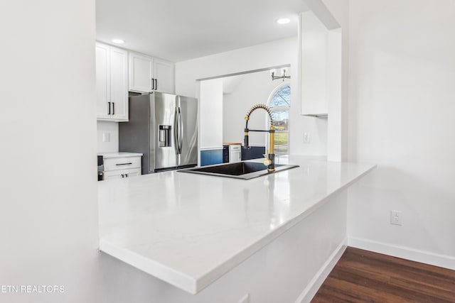 kitchen featuring a peninsula, dark wood-style flooring, a sink, white cabinets, and stainless steel fridge