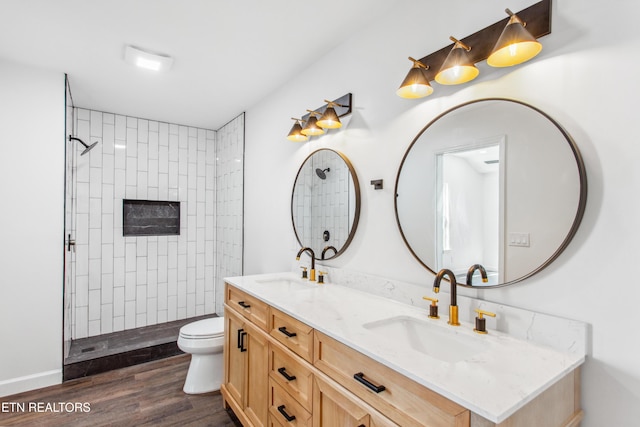 bathroom featuring tiled shower, toilet, wood finished floors, and a sink