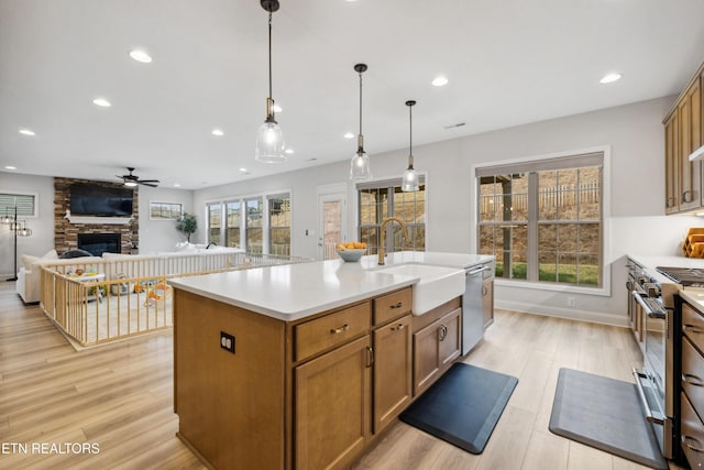 kitchen featuring light wood-style flooring, appliances with stainless steel finishes, a fireplace, a ceiling fan, and a sink