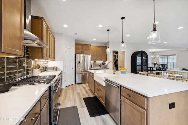 kitchen with light wood-style flooring, a sink, stainless steel appliances, wall chimney range hood, and a notable chandelier