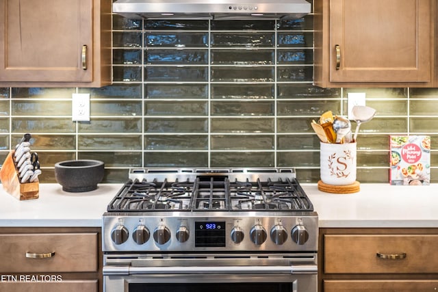 kitchen featuring brown cabinetry, decorative backsplash, light countertops, wall chimney range hood, and stainless steel gas stove