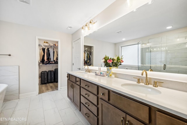 full bathroom with a spacious closet, a stall shower, a soaking tub, marble finish floor, and a sink