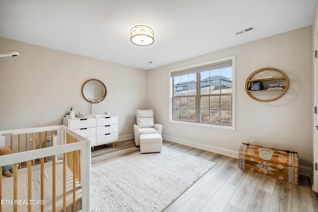 bedroom with a nursery area, wood finished floors, visible vents, and baseboards