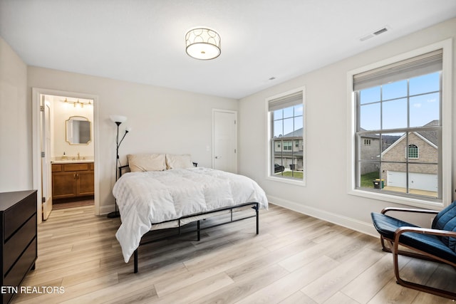 bedroom featuring baseboards, visible vents, ensuite bath, a sink, and light wood-type flooring