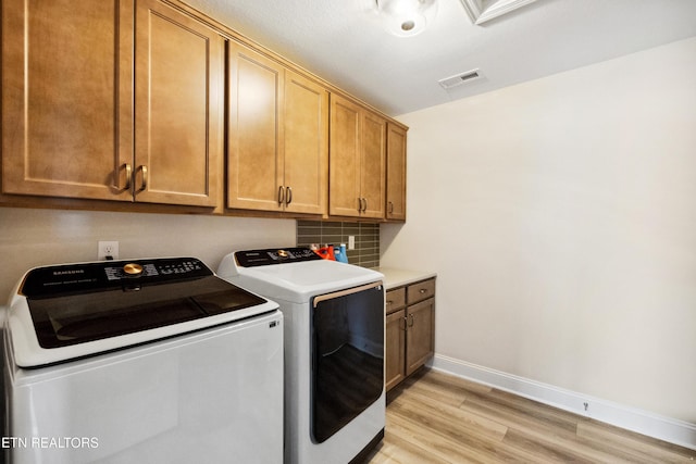 clothes washing area featuring visible vents, light wood-type flooring, washer and dryer, cabinet space, and baseboards