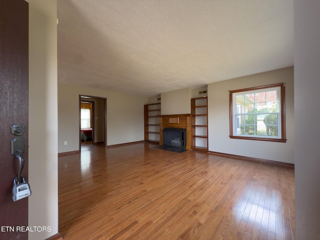 unfurnished living room with plenty of natural light, light wood-type flooring, a fireplace with flush hearth, and a textured ceiling