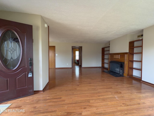 foyer entrance with light wood finished floors, visible vents, a textured ceiling, and baseboards